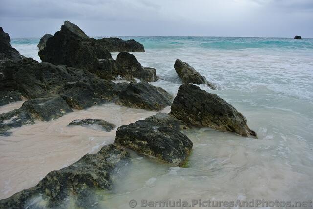 Black rocks battered by waves at Horseshoe Bay Beach.jpg